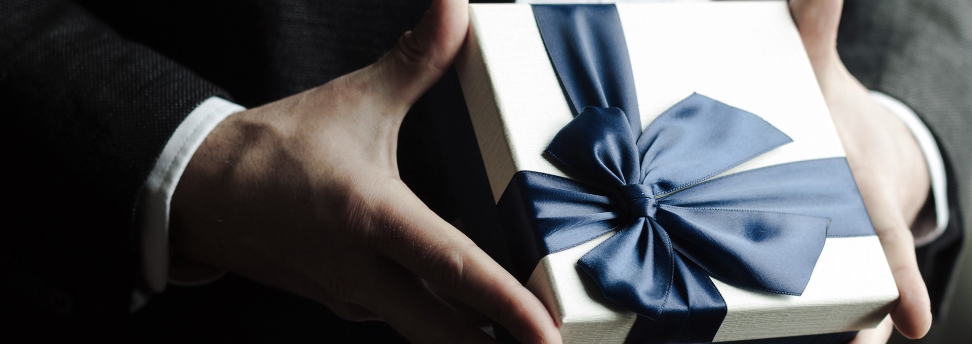 Gift box with large bow held in hands 