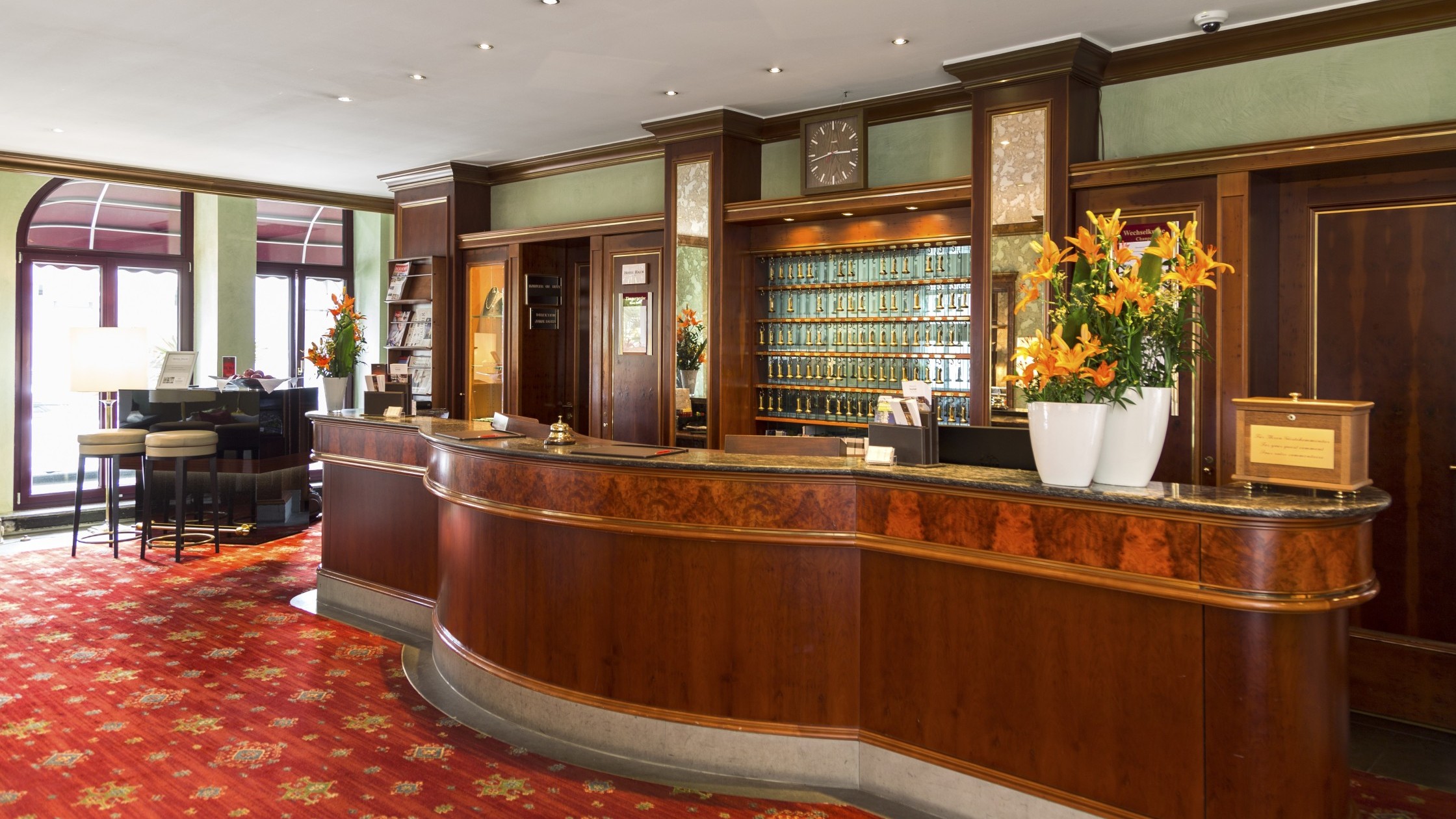 Hotel reception with elegant wood paneling, red carpet and golden room keys.