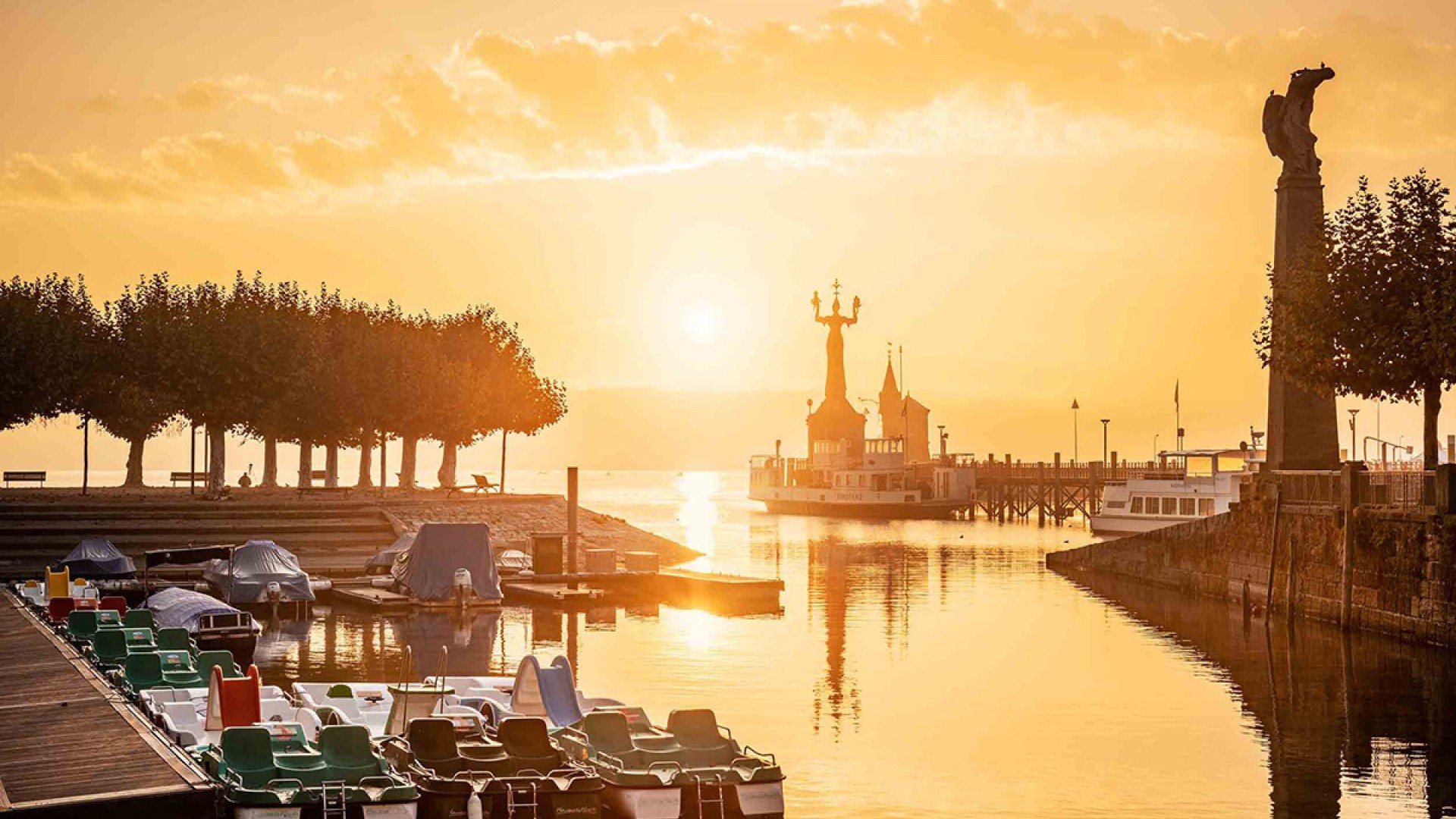 Gondelehafen in Constance glowing in the warm light of sunset, with boat docks and the historic Konzil in the background.