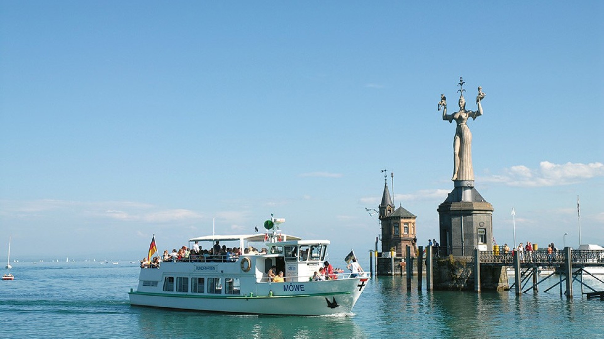 The passenger ship Möwe approaches the harbor entrance of Constance, surrounded by the picturesque backdrop of Lake Constance and the city.