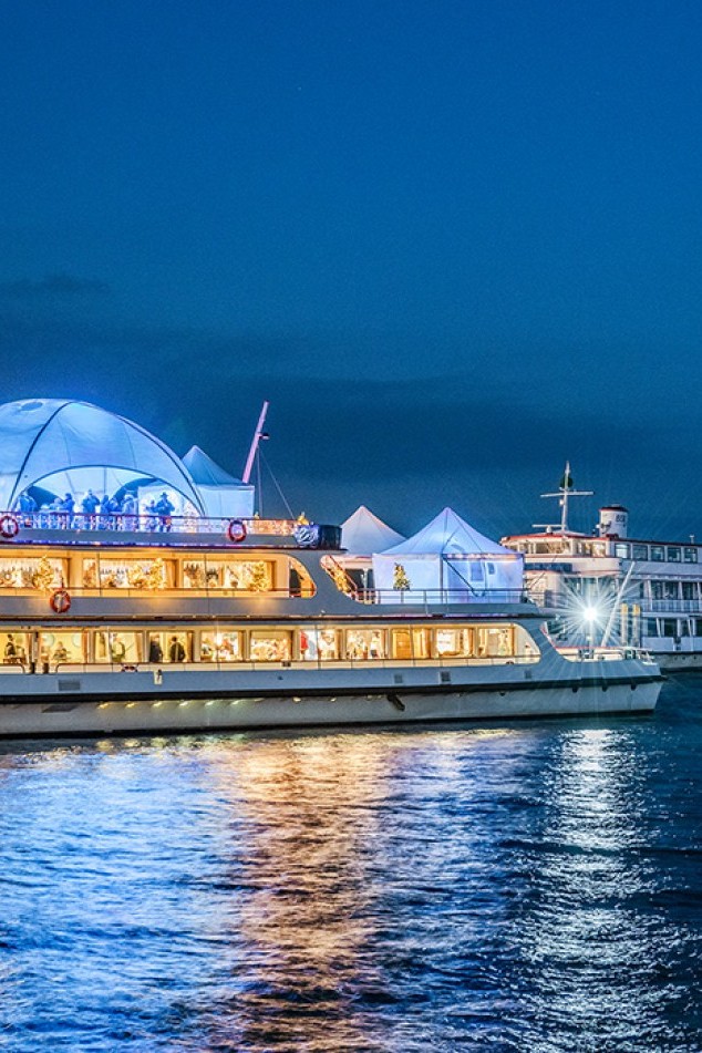 A festively decorated boat serving as an IceBar at the Christmas market in Konstanz, surrounded by lights and visitors.
