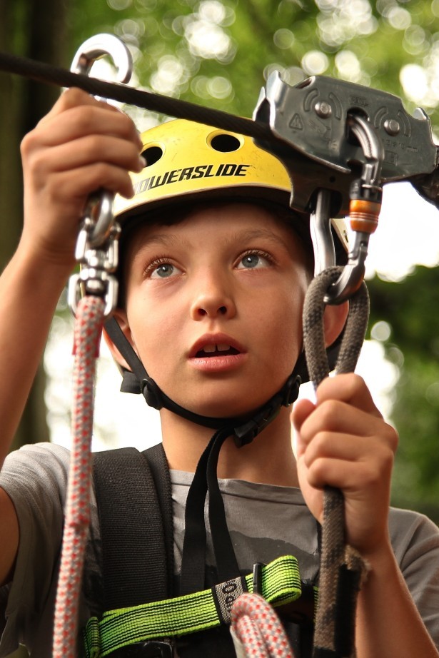 A boy hanging on a climbing wall, looking upwards.