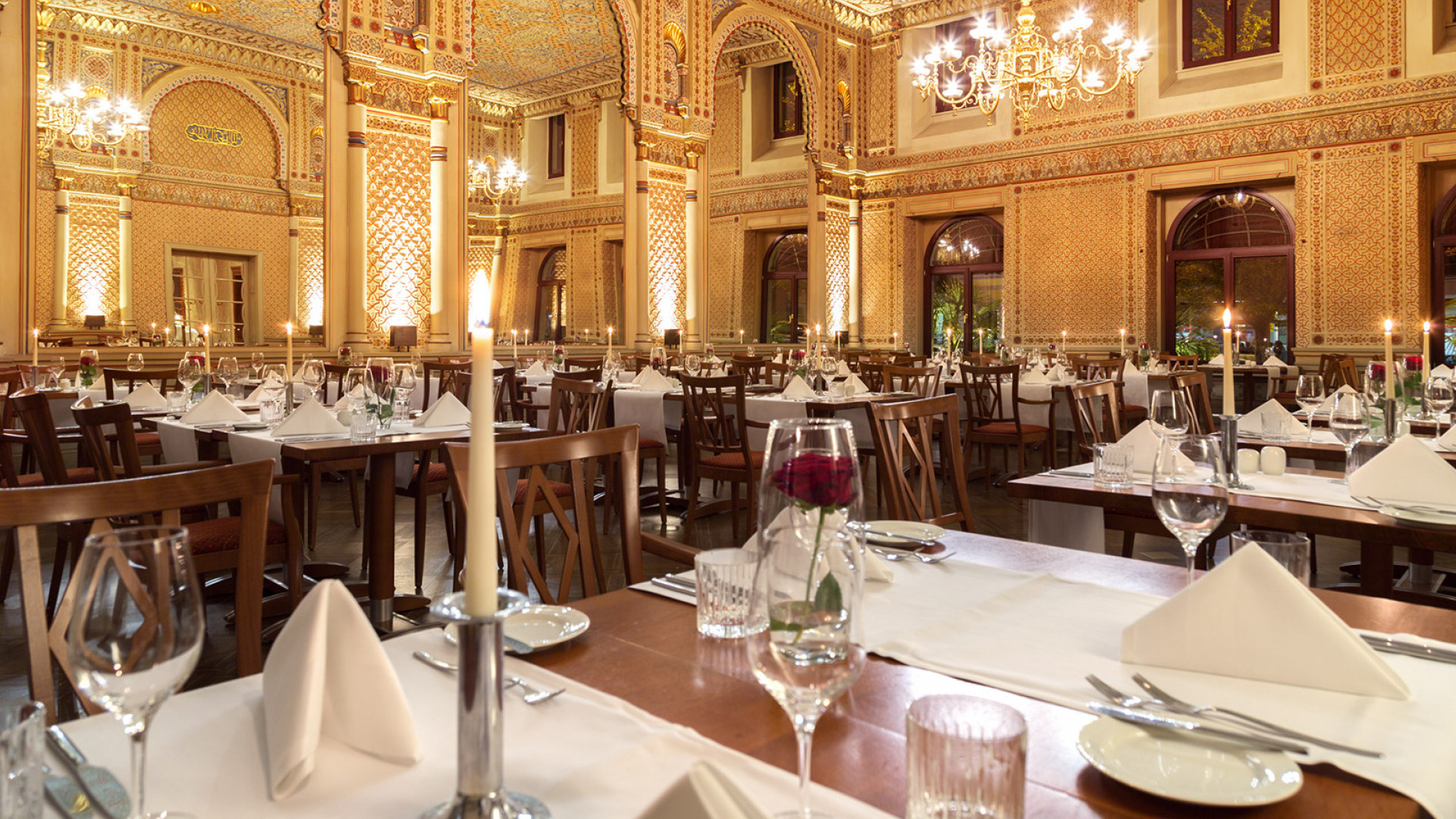  Gedeckte Tische mit roten Rosen und Kerzen im festlichen maurischen Saal, mit Blick auf die gigantischen Spiegeln und die wundervolle Wanddekoration. 