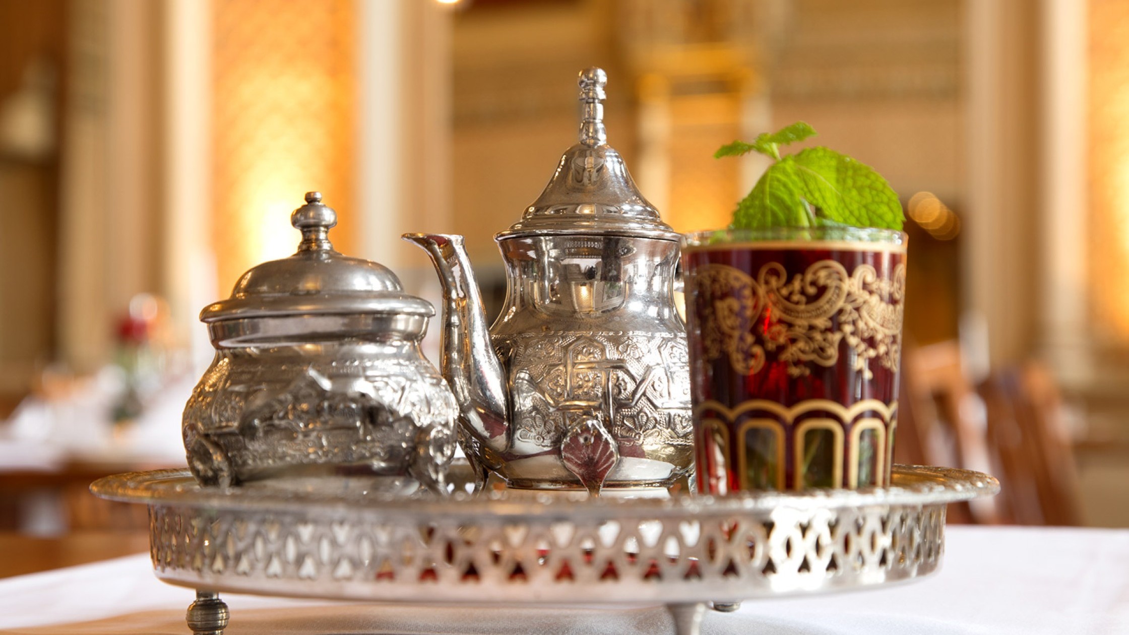 Moorish tea set with silver tray, silver sugar bowl with lid, small silver teapot and a red -patterned tea glass with fresh mint.