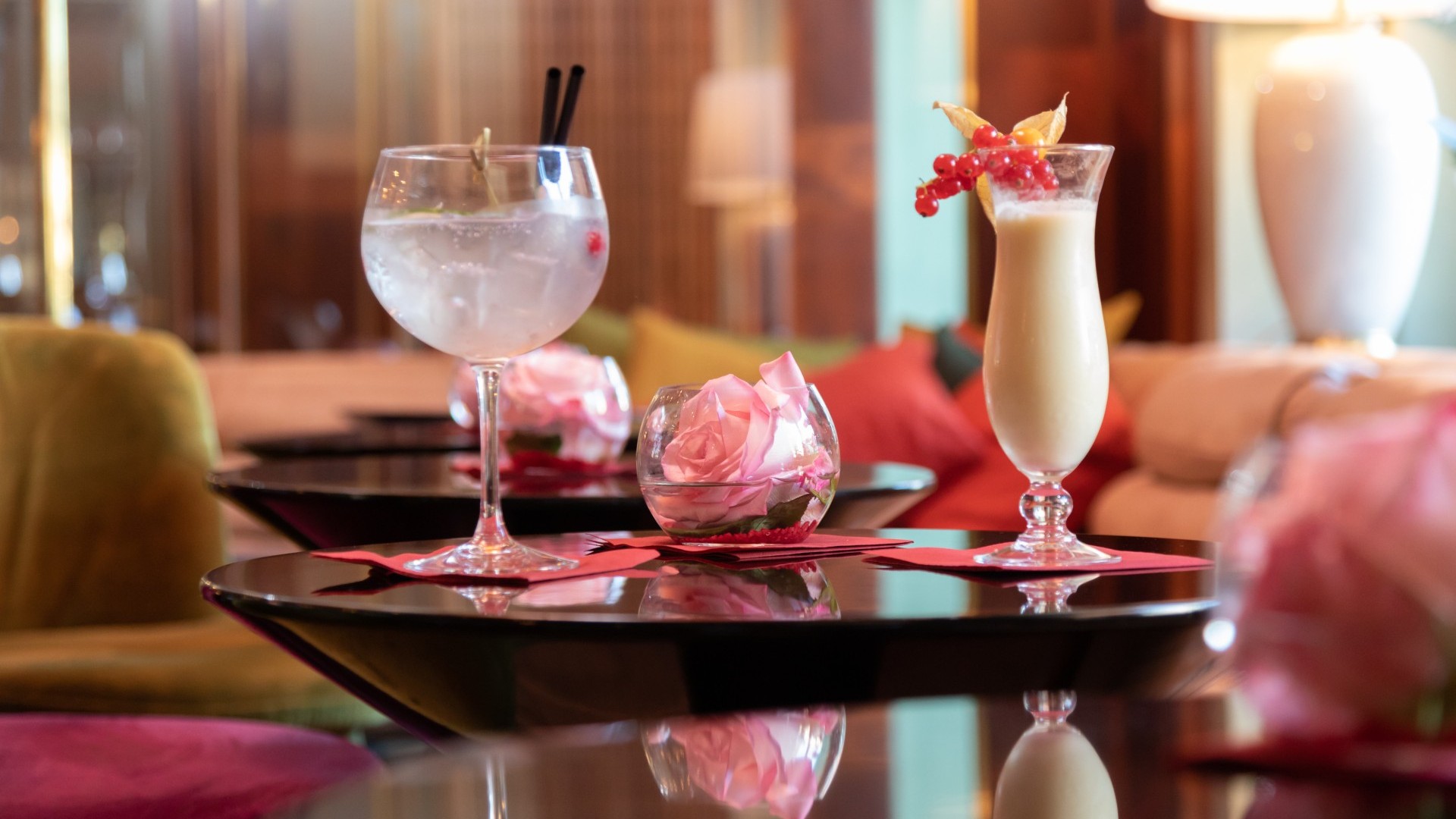 Pina Colada und Gin Tonic auf einem Tisch mit frischer Rose in einer Glasschale in der gemütlichen Hotelbar. 
