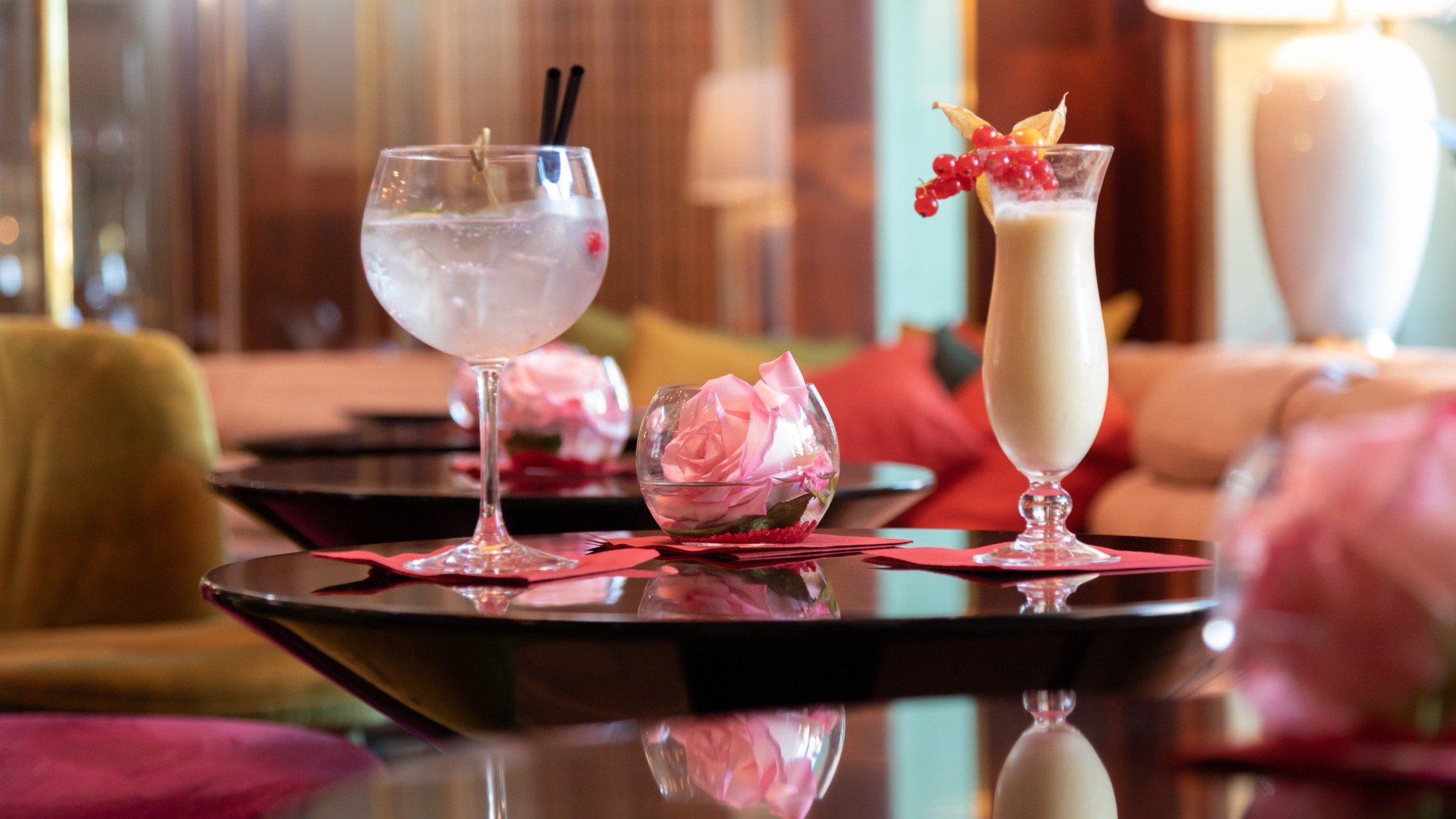 Pina colada and gin and tonic on a table with a fresh rose in a glass bowl in the cozy hotel bar.