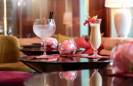 Pina colada and gin and tonic on a table with a fresh rose in a glass bowl in the cozy hotel bar.