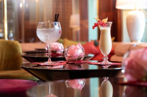 Pina colada and gin and tonic on a table with a fresh rose in a glass bowl in the cozy hotel bar.