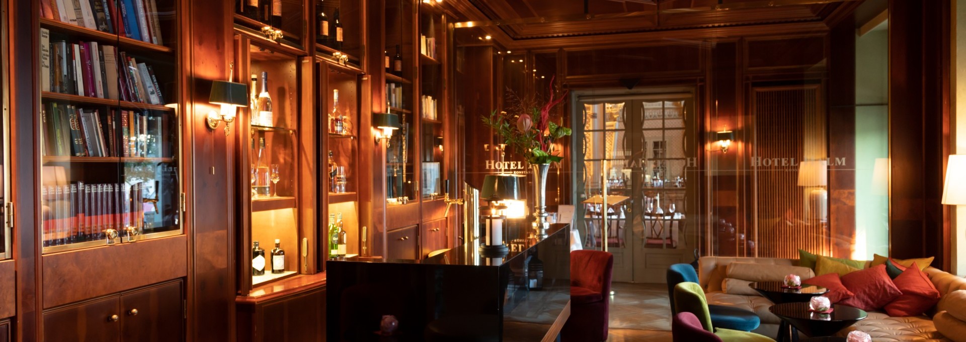 Hotelbar mit beleuchtetn Regalen voller Büchern, verziehrter Holzdecke und gemülichen Sitzgelegenheiten. 