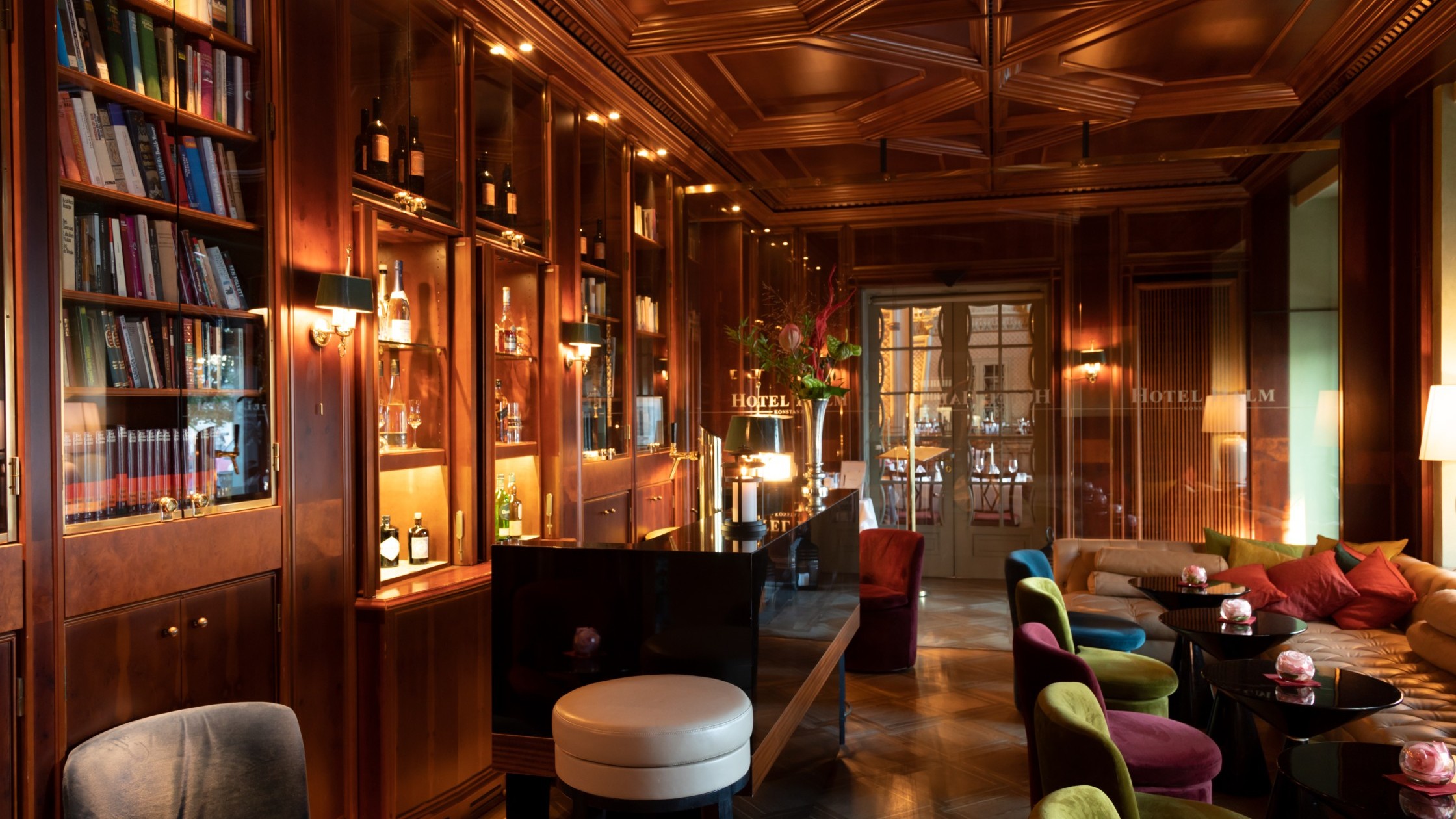 Hotel bar with illuminated shelves full of books, decorated wooden ceiling and cozy seating.