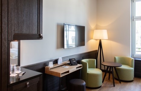 Modernly furnished hotel room with double bed, marble bathroom, and cozy seating area 