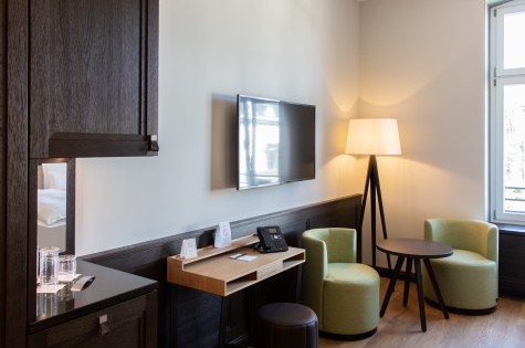 Modernly furnished hotel room with double bed, marble bathroom, and cozy seating area 